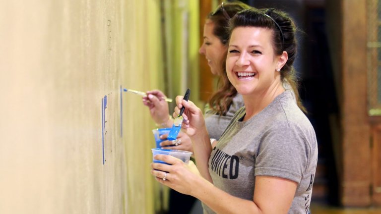 Woman smiling at camera while painting a wall