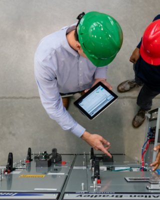 Dos empleados en la fábrica viendo una tableta frente a un producto de Rockwell Automation