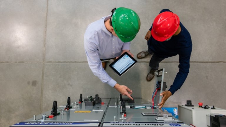 两名工厂员工站在罗克韦尔自动化产品前查看平板电脑