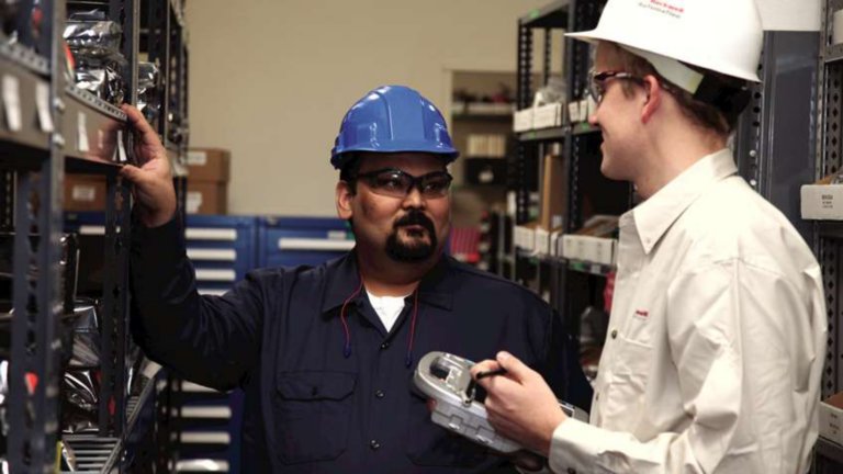 Dos empleados de Rockwell Automation parados en un pasillo con estanterías en una planta