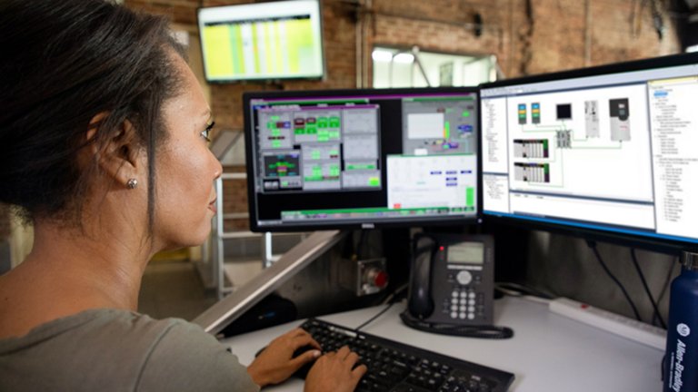 Dipendente di sesso femminile seduta alla propria scrivania che guarda vari monitor e inserisce informazioni in un’applicazione software 