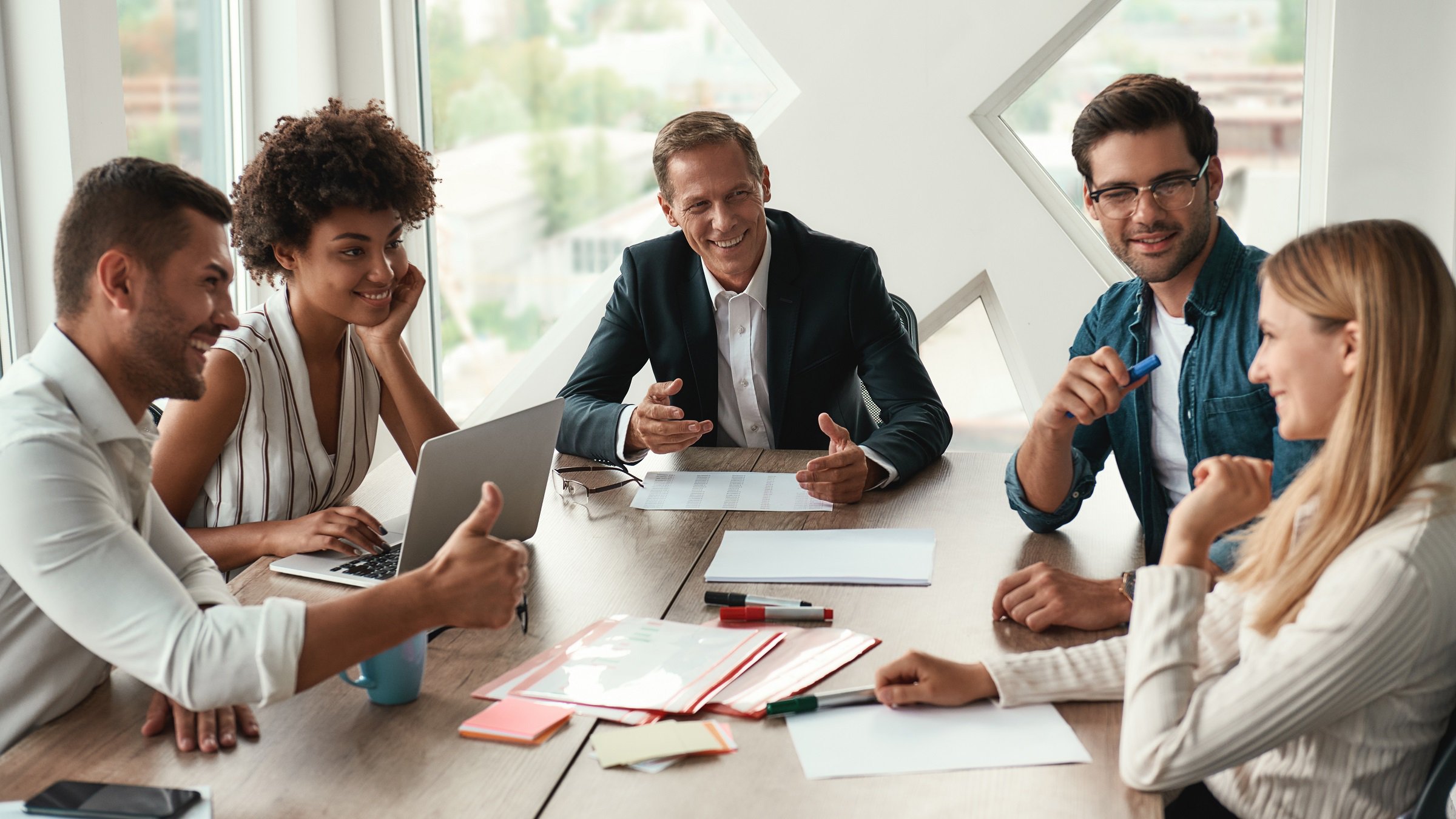 Teamwork. Multicultural team discussing something and smiling while sitting at the office table