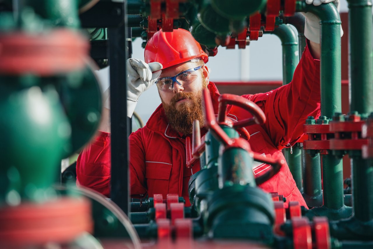 Oil and gas engineer in red jumpsuit working on pipeline equipment. 