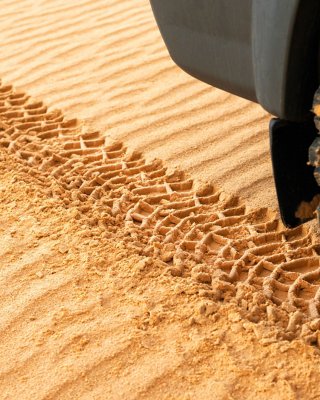 Close de um veículo em movimento deixando rastros na areia