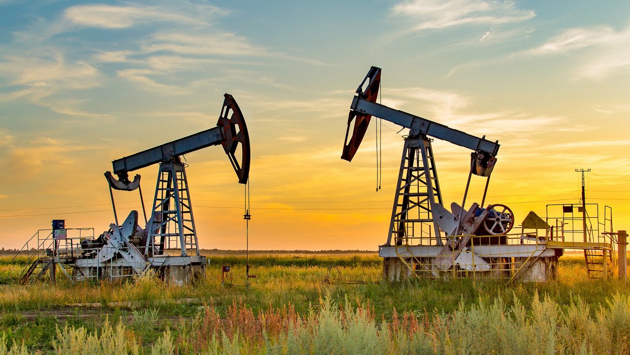 Vista di un campo petrolifero e di Oil & Gas onshore in attività, con un primo piano di due pompe al tramonto.