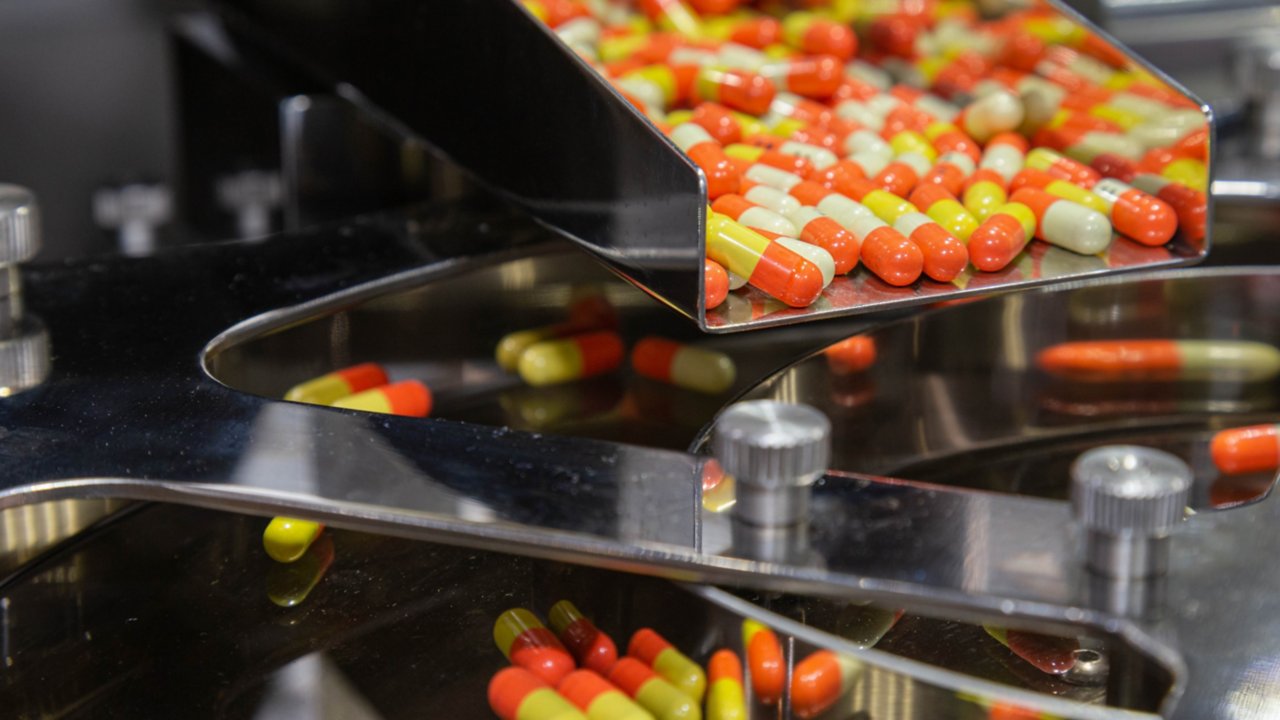 Eine Reihe mehrfarbiger Pillen bewegen sich eine Metallrutsche hinunter, die Teil der Produktionslinie eines Life-Sciences-Herstellers ist.