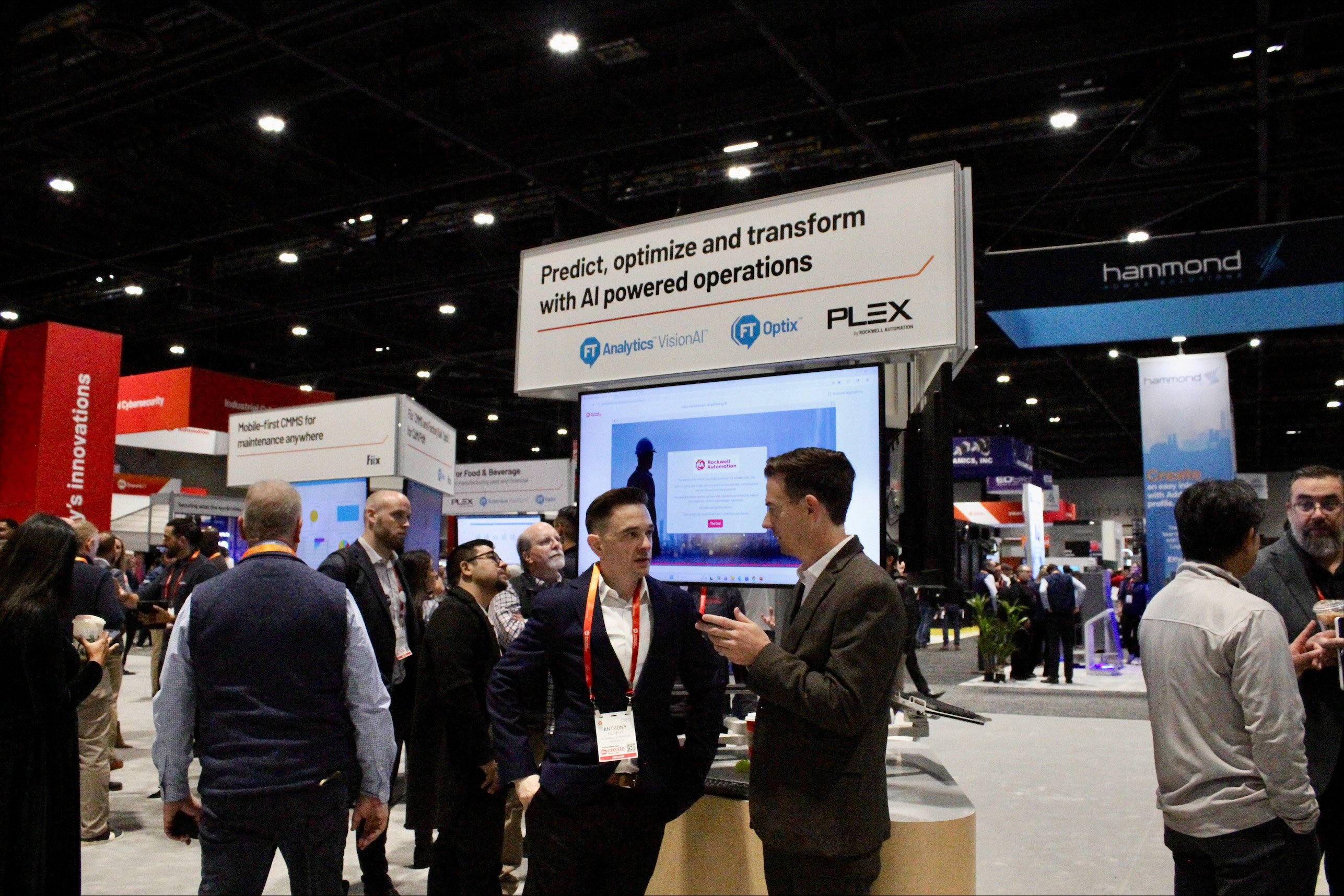 Expo booth with a sign reading ‘Predict, optimize and transform with AI powered operations’ and attendees gathered around a display