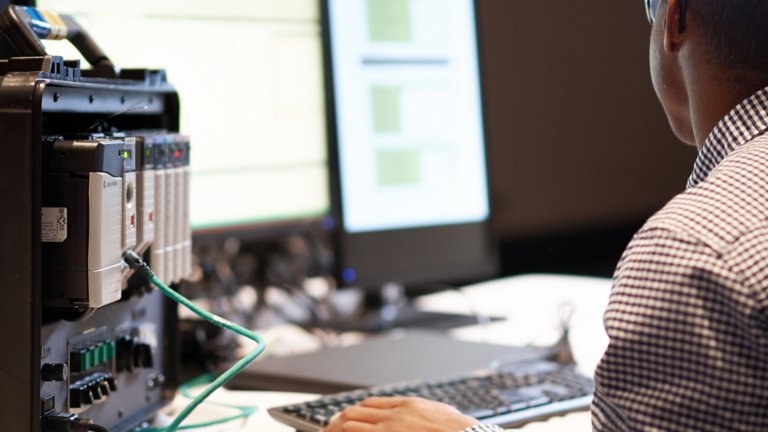 Un empleado en su escritorio viendo software de visualización en su monitor y un producto enchufado a su computadora portátil a través de un cable de red