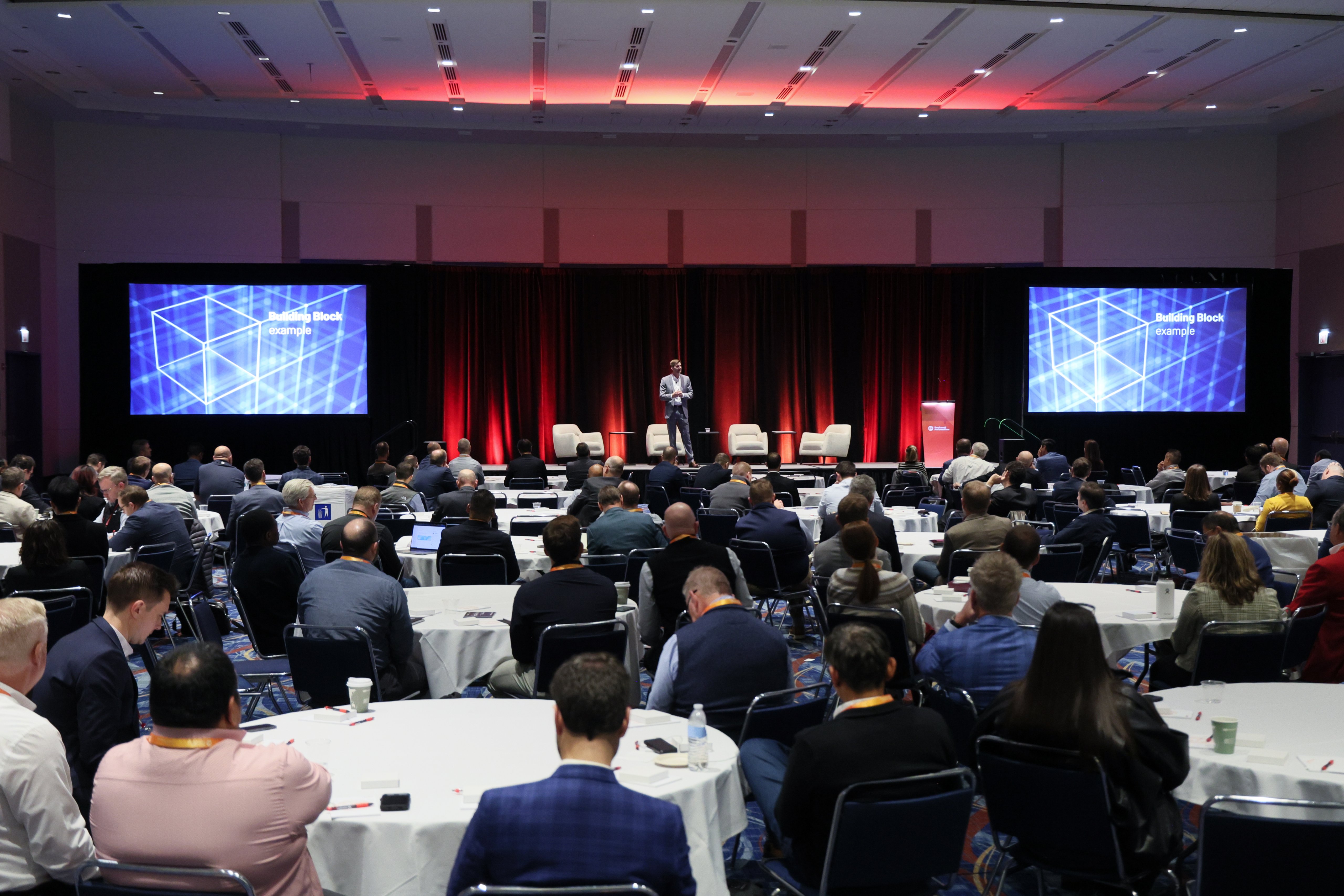 A room with tables of people and a presenters on stage