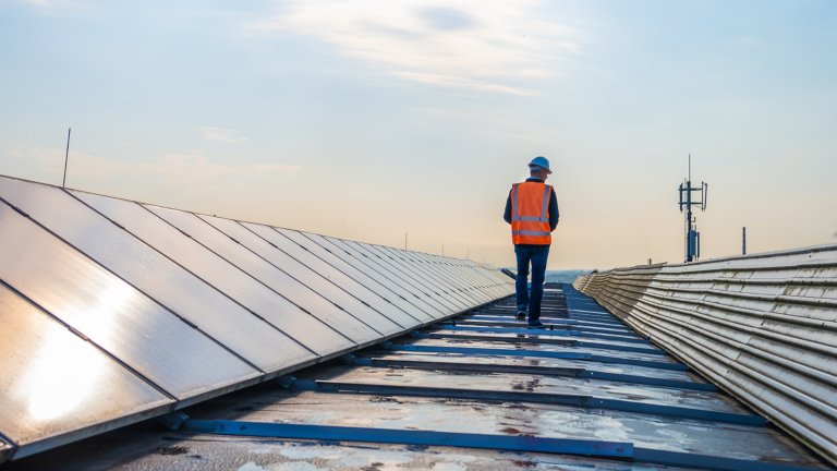 A worker in an orange high visibility vest walking past a row of solar panels