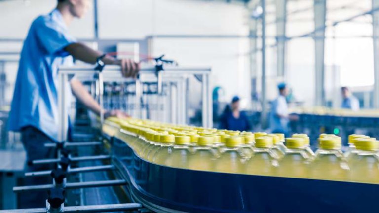 Männlicher Mitarbeiter steht an einem Förderband, das Flaschen in einer Fabrik bewegt