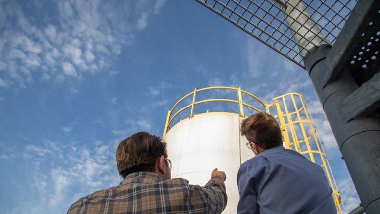 two men looking up at a water tank with blue sky and clouds in the background