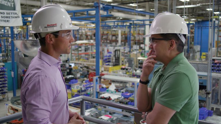 Two male Rockwell Automation employees wearing hard hats in deep discussion on the mezzanine inside the factory