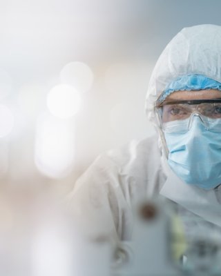 Due operatori del Life Sciences che indossano tute, maschere e occhiali di sicurezza interagiscono con le attrezzature di produzione farmaceutica all’interno di un impianto ben illuminato.