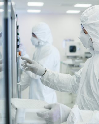 A life sciences professional wearing coveralls, a mask and safety glasses examines an automated pharmaceutical production line inside a manufacturing facility.