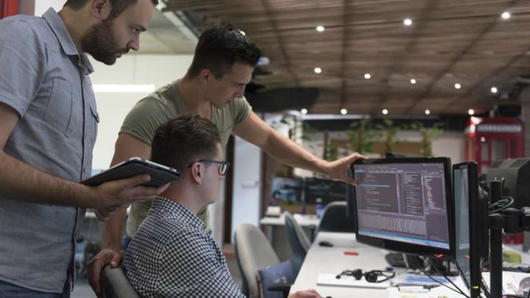 Três funcionários observando o software em um monitor na estação de trabalho de um funcionário