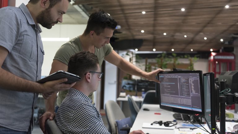 Tres empleados ven software en un monitor en el escritorio de uno de ellos