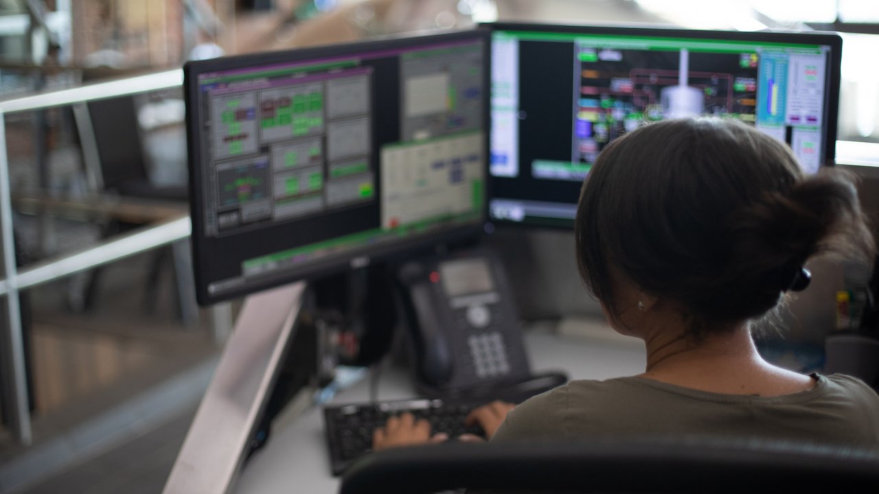 Funcionária em sua estação de trabalho observando um monitor que exibe o software e digitando informações no programa