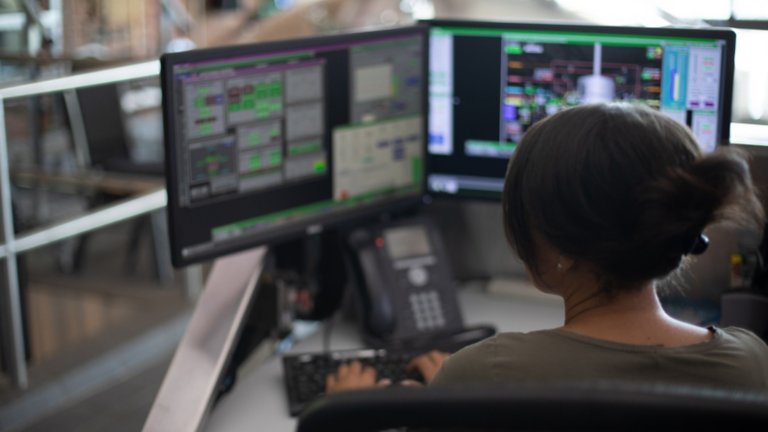 Una empleada en su escritorio con una computadora en la que se visualiza el software y escribiendo información en el programa de software