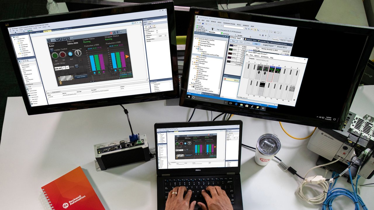Dipendente di sesso maschile che inserisce informazioni in Studio 5000 View Designer sul suo laptop con altri due monitor che visualizzano diverse schermate del software