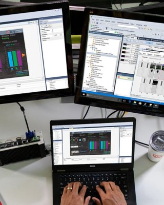 Un empleado que ingresa información en Studio 5000 View Designer en su computadora portátil con otros dos monitores que muestran diferentes pantallas de software