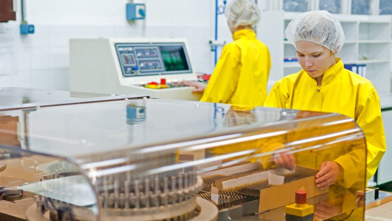 Two people wearing yellow jackets and hair nets in a pharmaceutical company