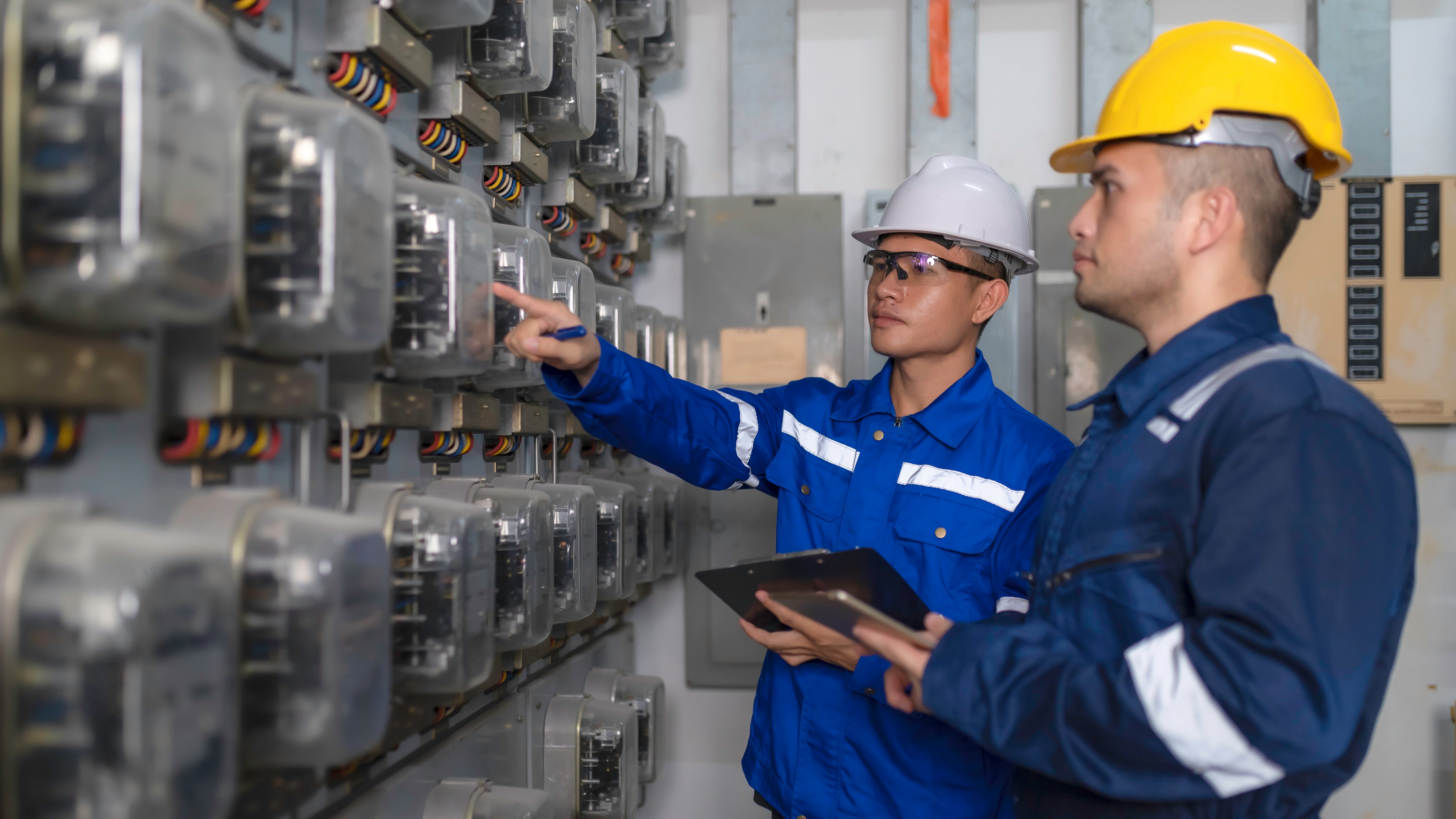 Los ingenieros y técnicos eléctricos trabajan juntos para resolver los fallos del sistema eléctrico en las salas de control industrial. El supervisor realiza mantenimiento del gabinete de circuitos y comprueba el panel de medidores eléctricos de la planta industrial.