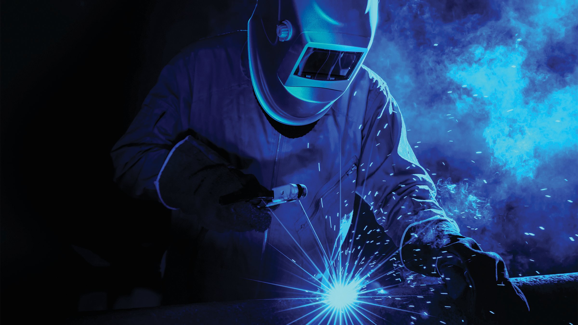 Welder at an industrial facility with blue sparks.