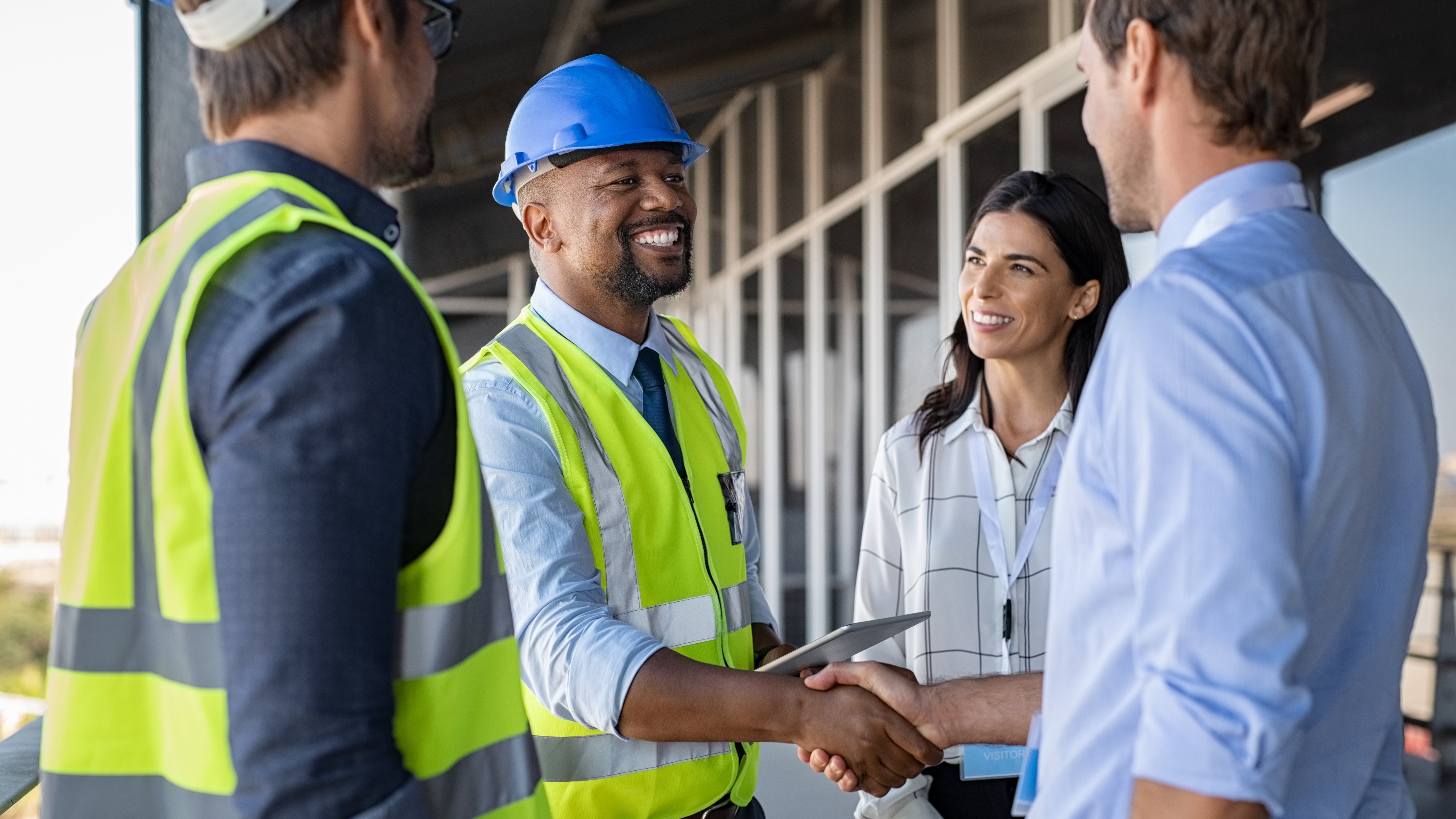 Smiling engineer shaking hands at construction site with happy architect. Handshake between cheerful african construction manager with businessman at bulding site. Team of workers with architects and contractor conclude an agreement with safety uniform.