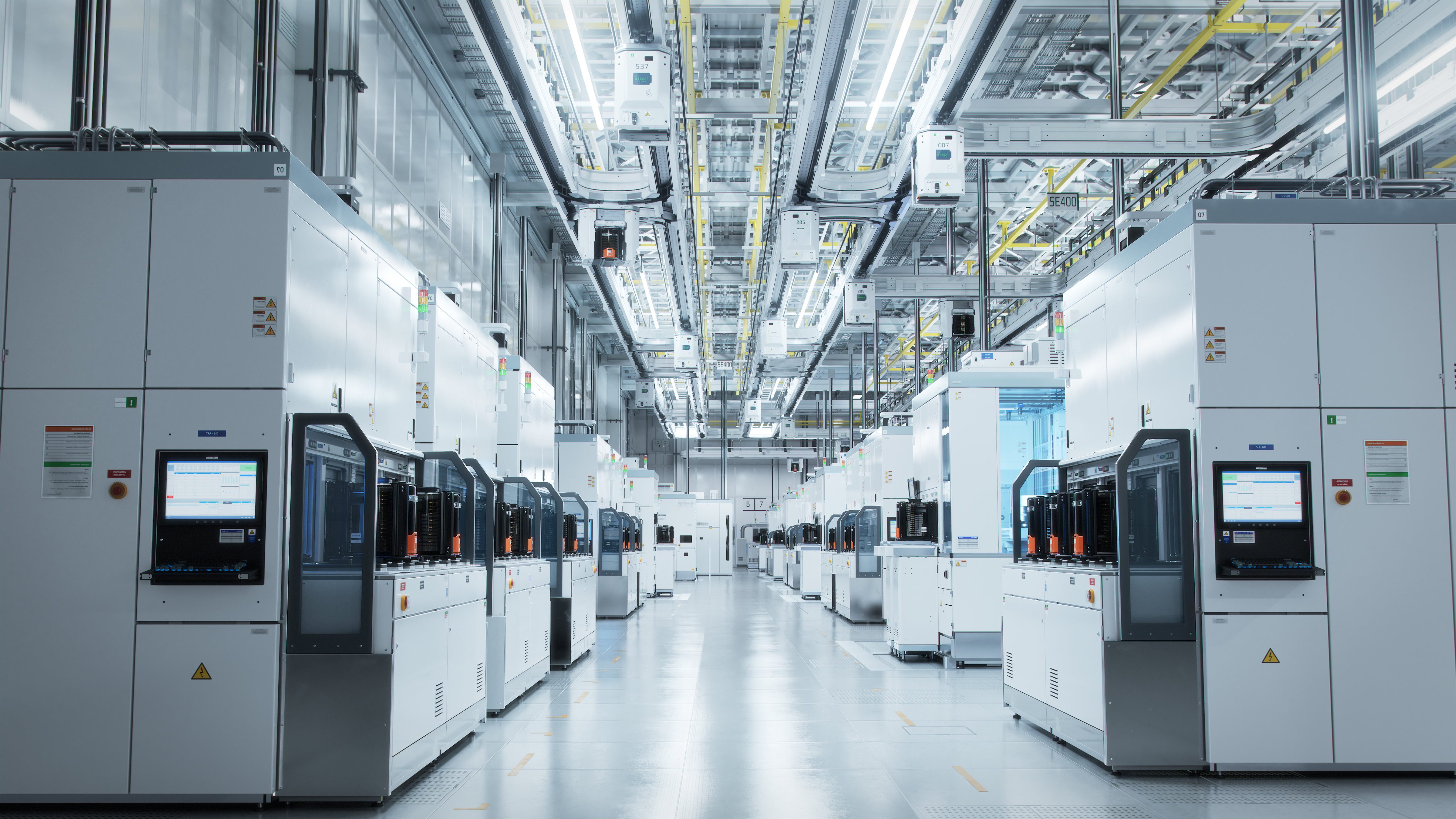 A wide shot of a hallway in a bright white advanced semiconductor production fab cleanroom, with overhead lights 