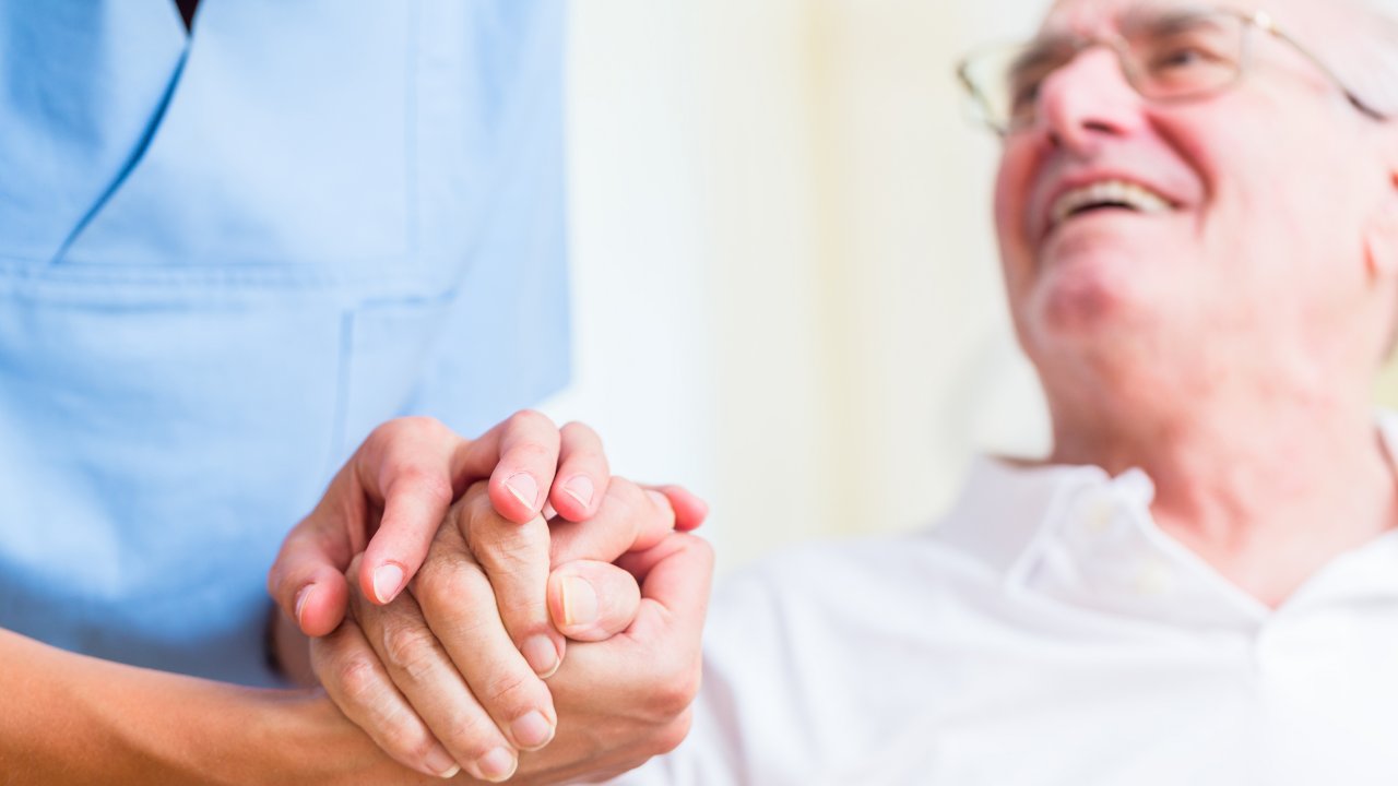 doctor standing by and holding hand of patient who is sitting and smiling looking up at doctor
