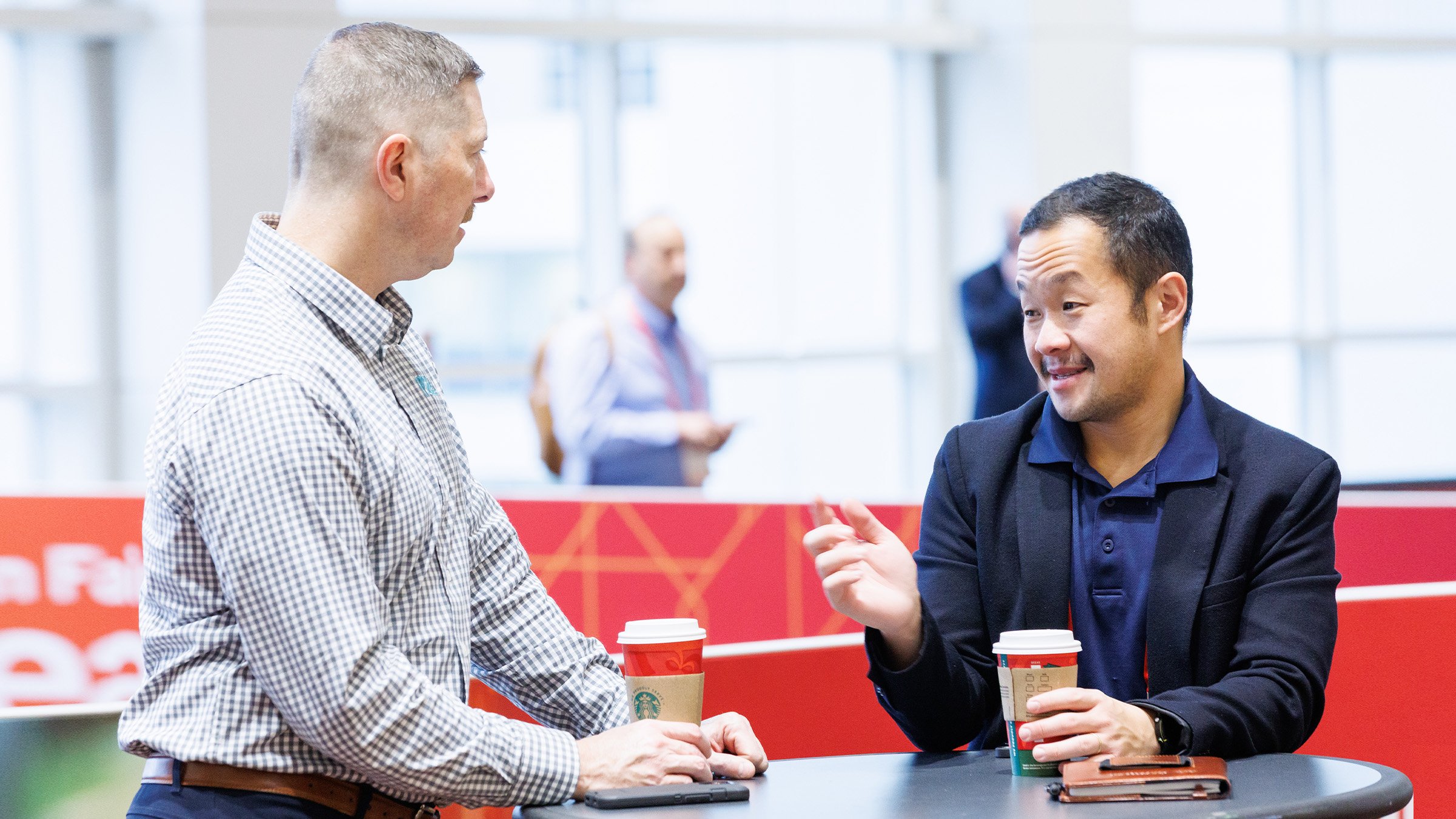 Two men chat at a table with coffee at an event