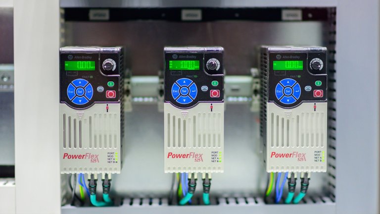 Three side-by-side Allen-Bradley VFD drives. Connected by multiple cables, these electronic variable frequency drives (VFDs) provide precise motor control for applications in factories and commercial buildings.