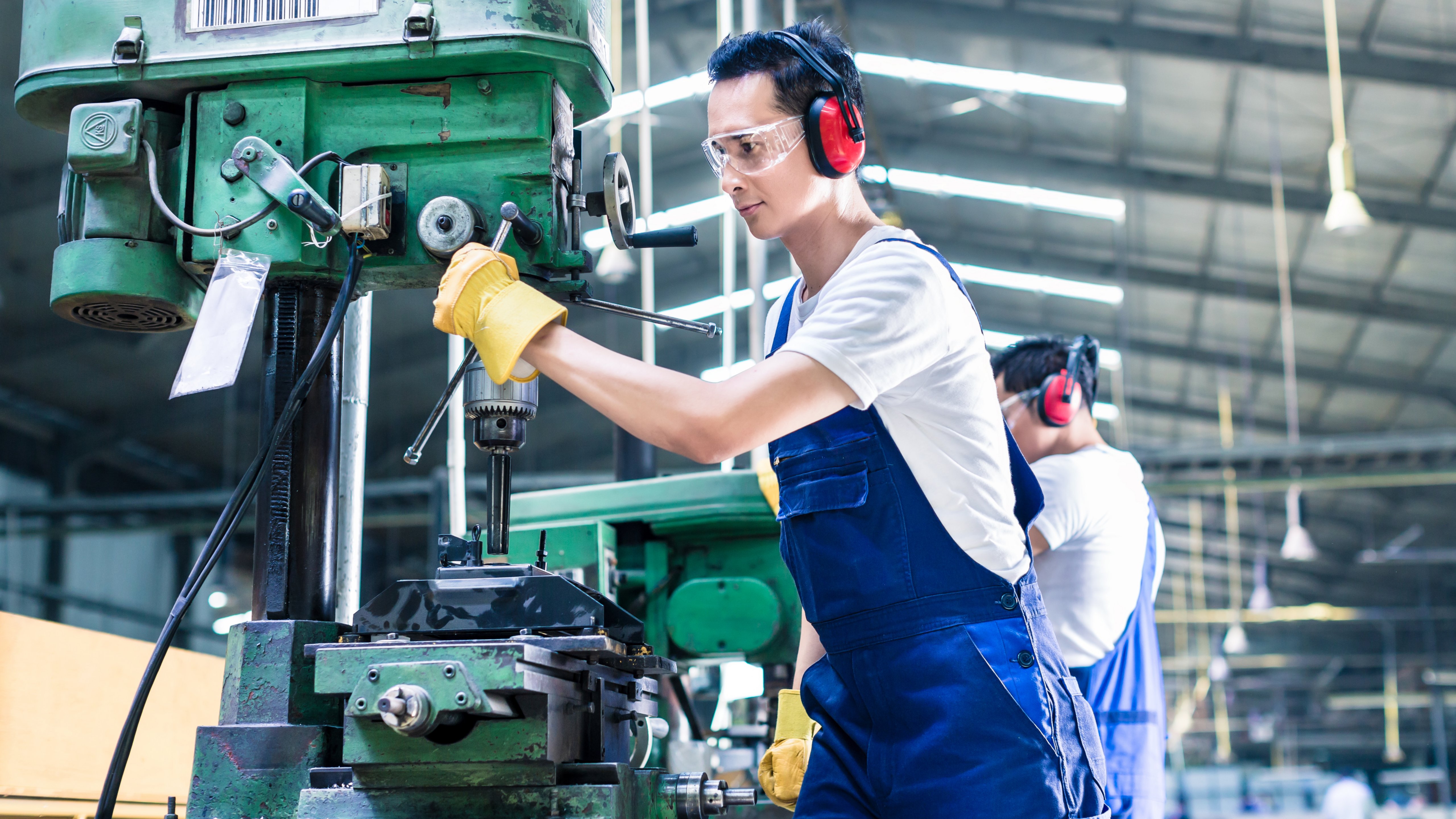 Asian worker in production plant drilling at machine on the factory floor