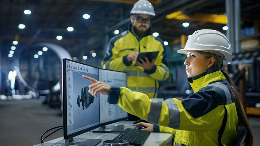 Trabajadores industriales en una sala de supervisión con doble pantalla