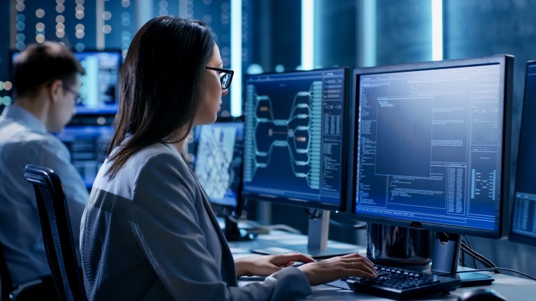 Two office workers siting beside each other typing on keyboards and viewing data on their monitors