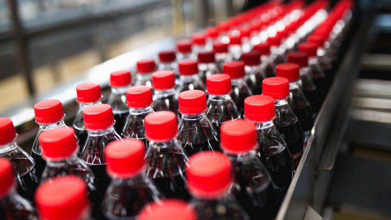 Bottling line of brand agnostic plastic bottles of soda with red caps and blurred out background