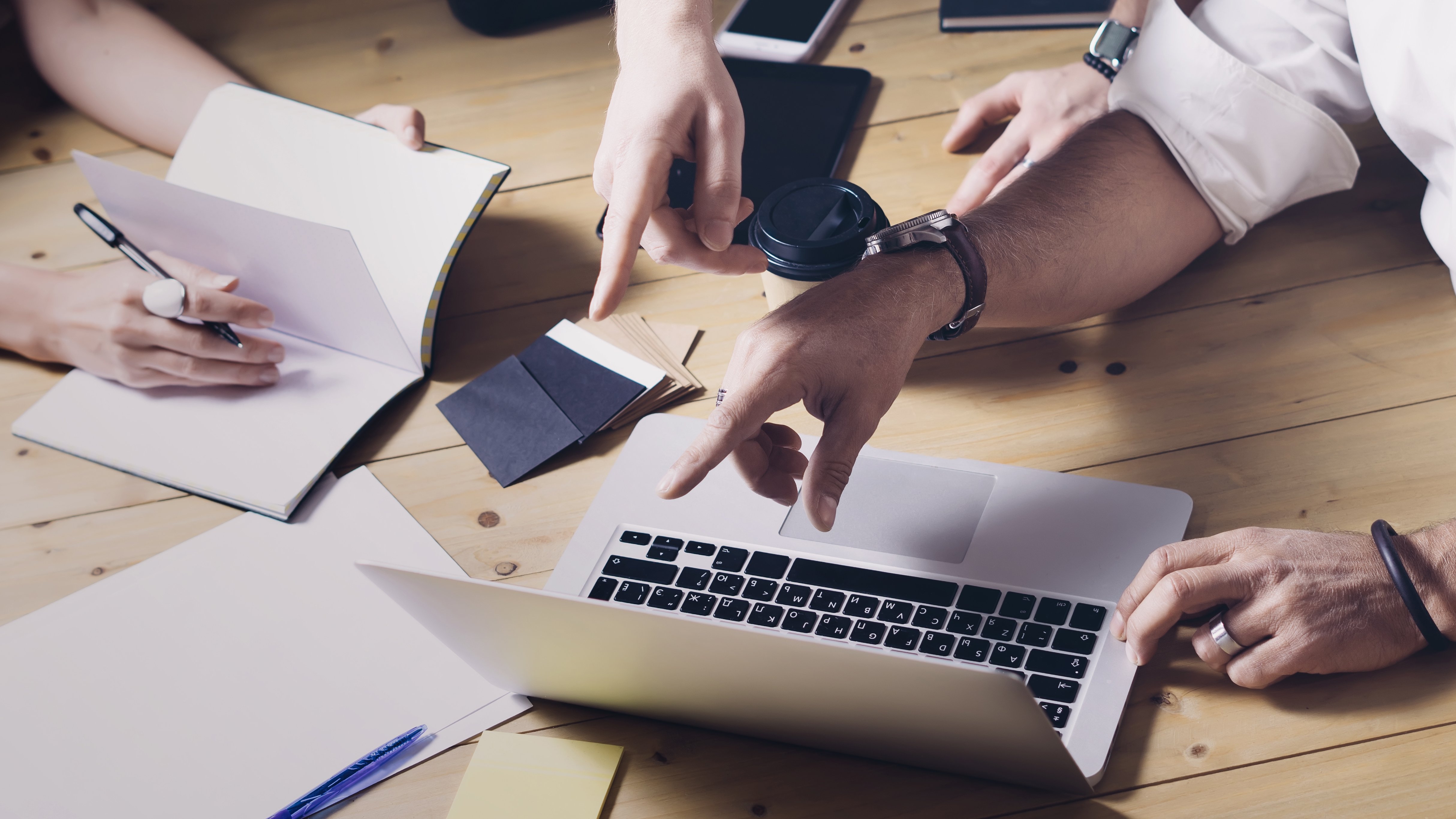 Hands pointing to laptop and writing into notepad