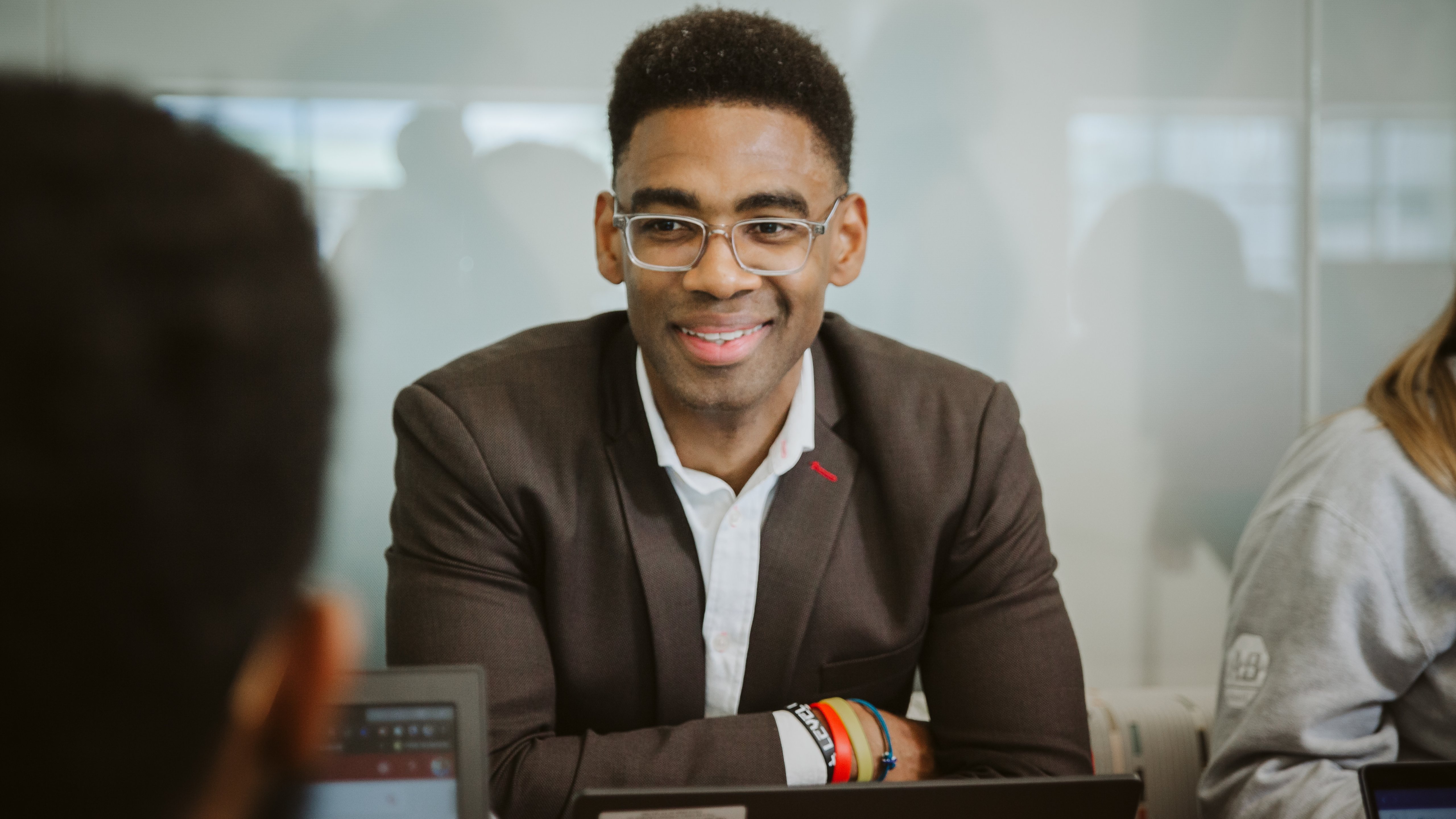 Man in a suit smiling at a meeting, laptop open in front of him