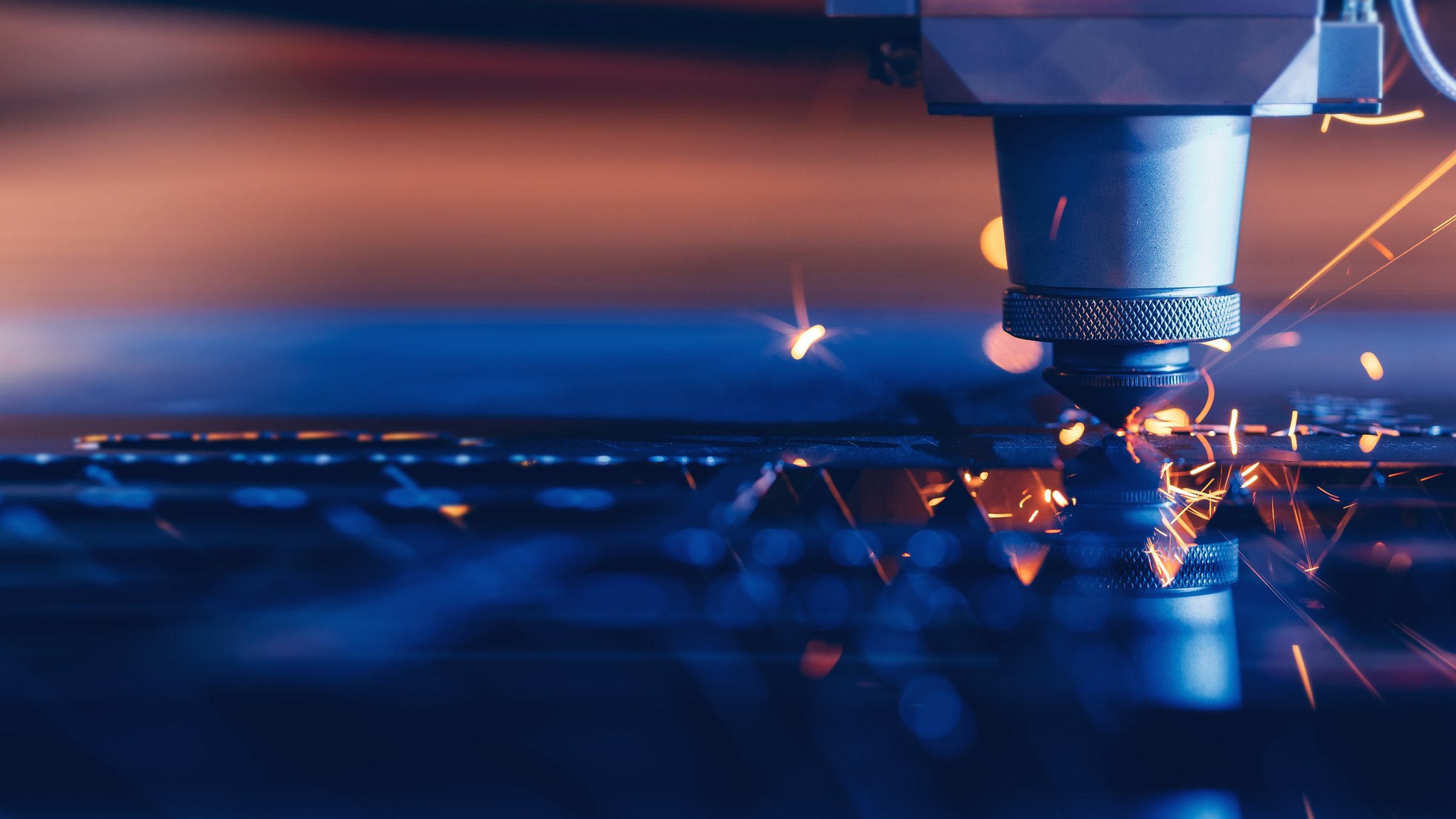 Photo of an industrial CNC laser cutting metal, with light sparks coming out. 