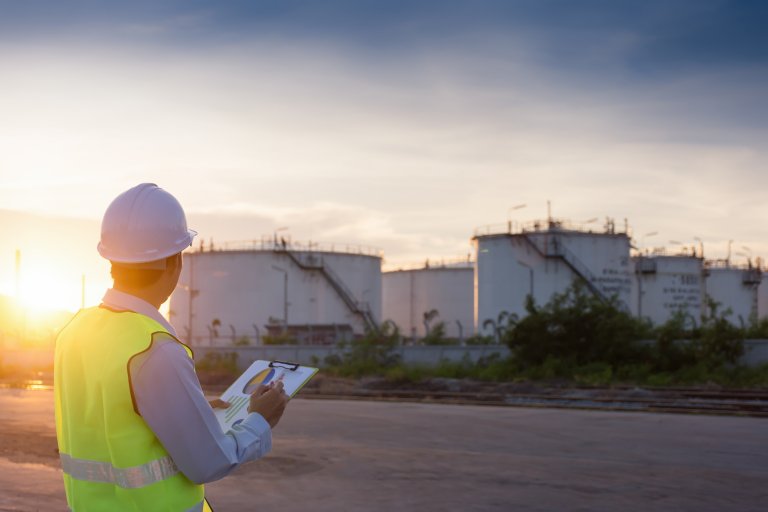 Engineer writing on the paper in front of the oil tank.Refinery, gas and oil