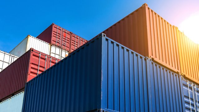 A close-up photos of multiple stacked metal shipping containers: red, blue, yellow, white.