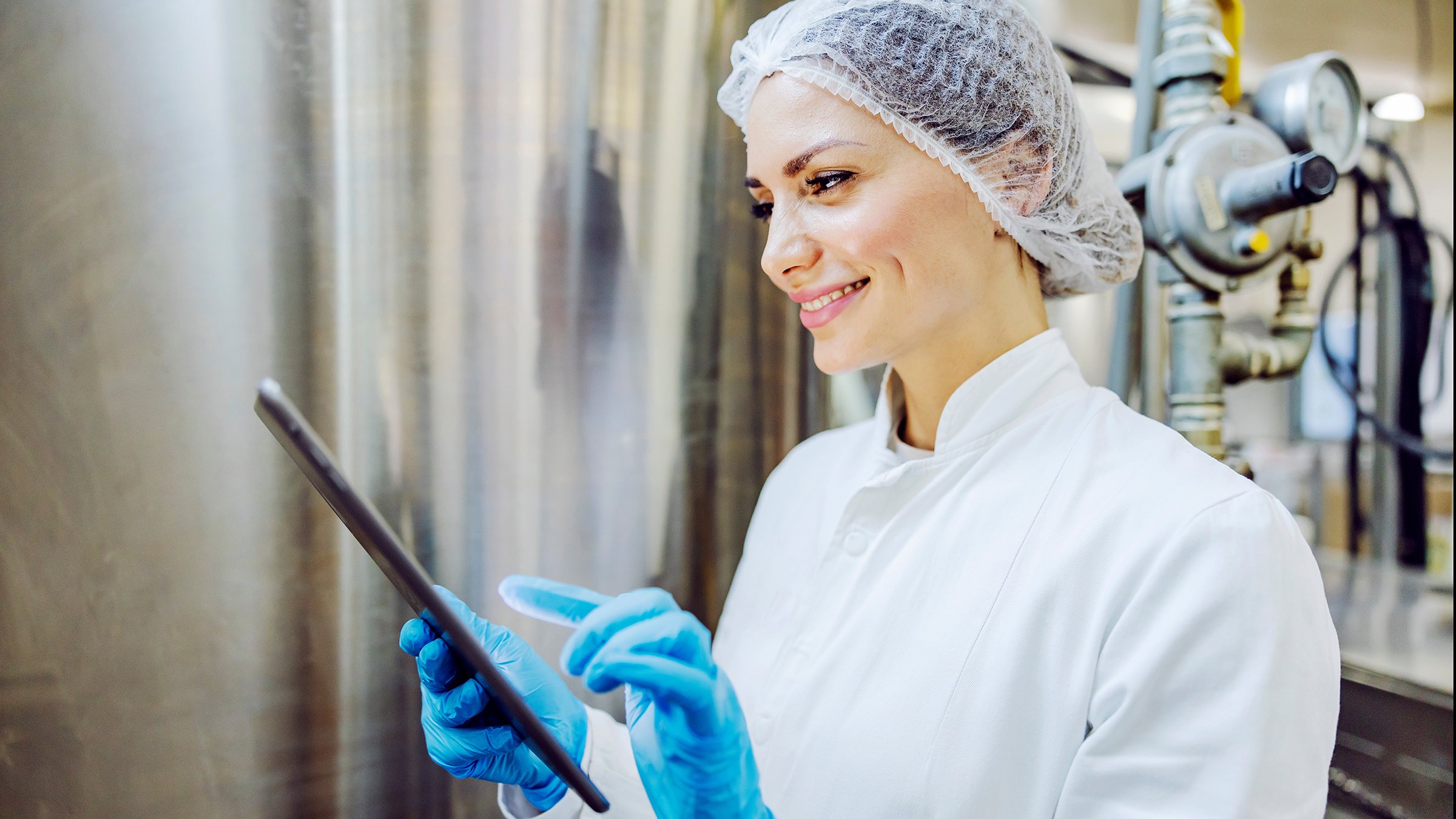 A female dairy factory worker smiling at the tablet and scrolling on it.