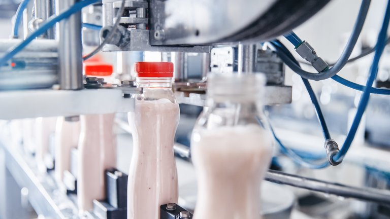 Producción de lácteos, una botella de yogur en una línea transportadora automatizada, proceso de llenado y envasado de leche.