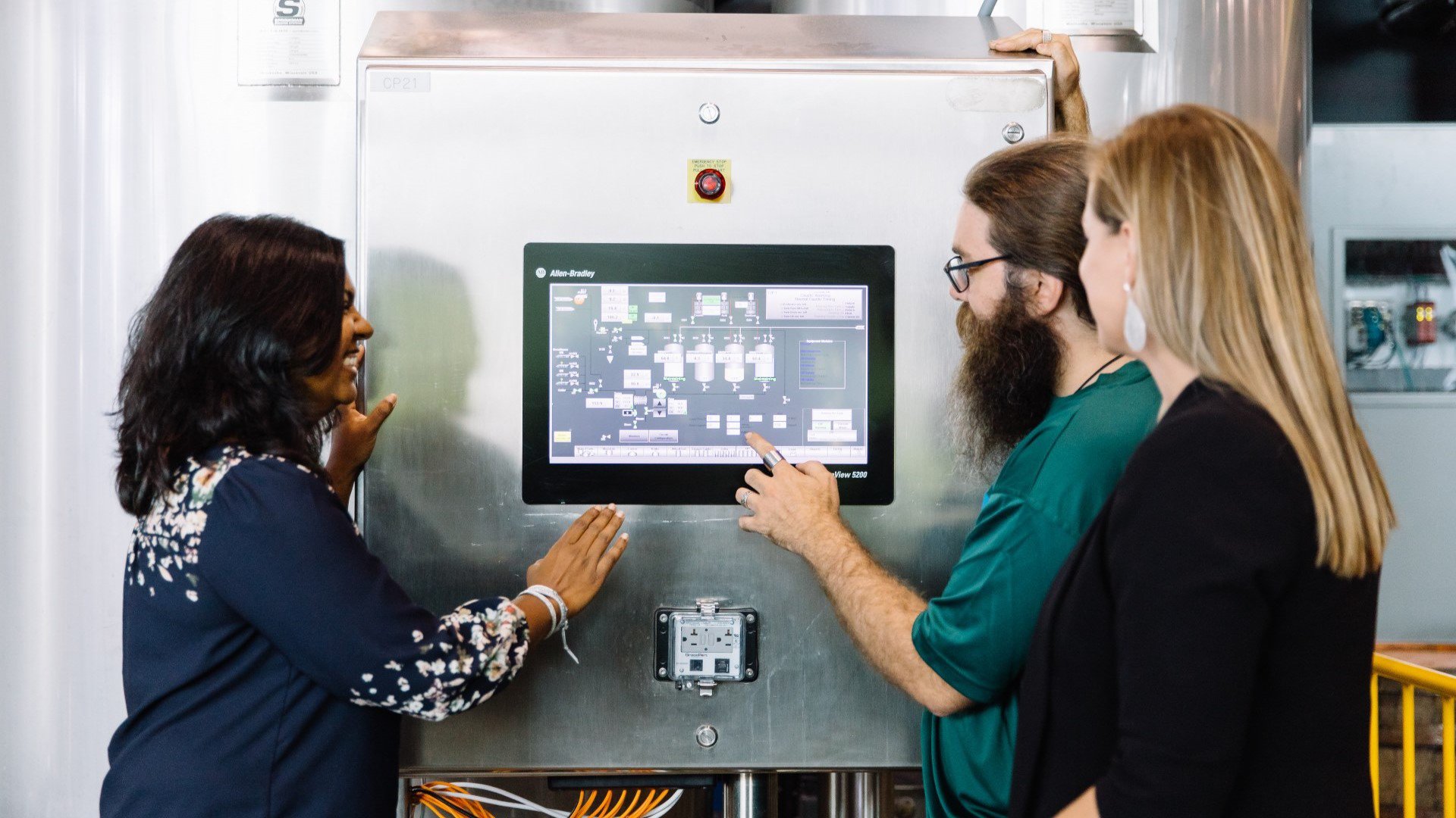 Tres trabajadores observando e interactuando con un panel táctil en sala de monitoreo industrial