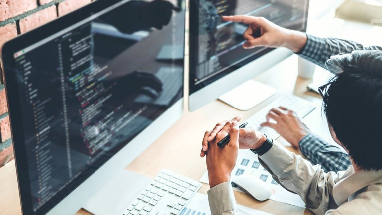 Development team works at a desk in an office, pointing at computer screens.