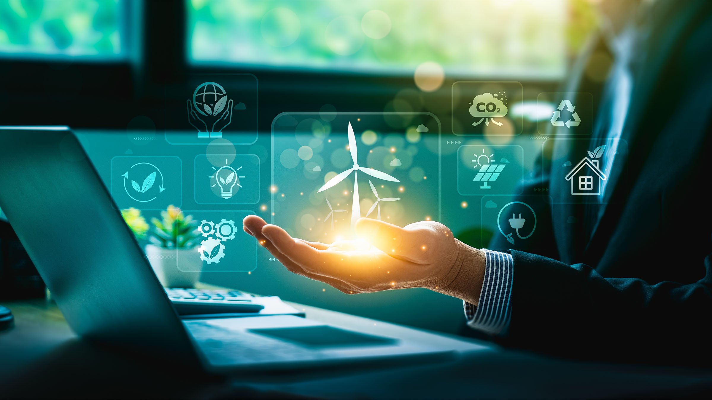 A digital icon of wind turbines sits in businessman’s hand with other green energy icons surrounding it.