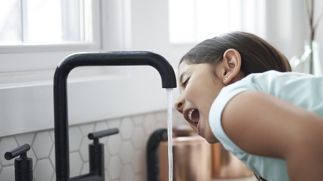 Young girl drinking water from a faucet