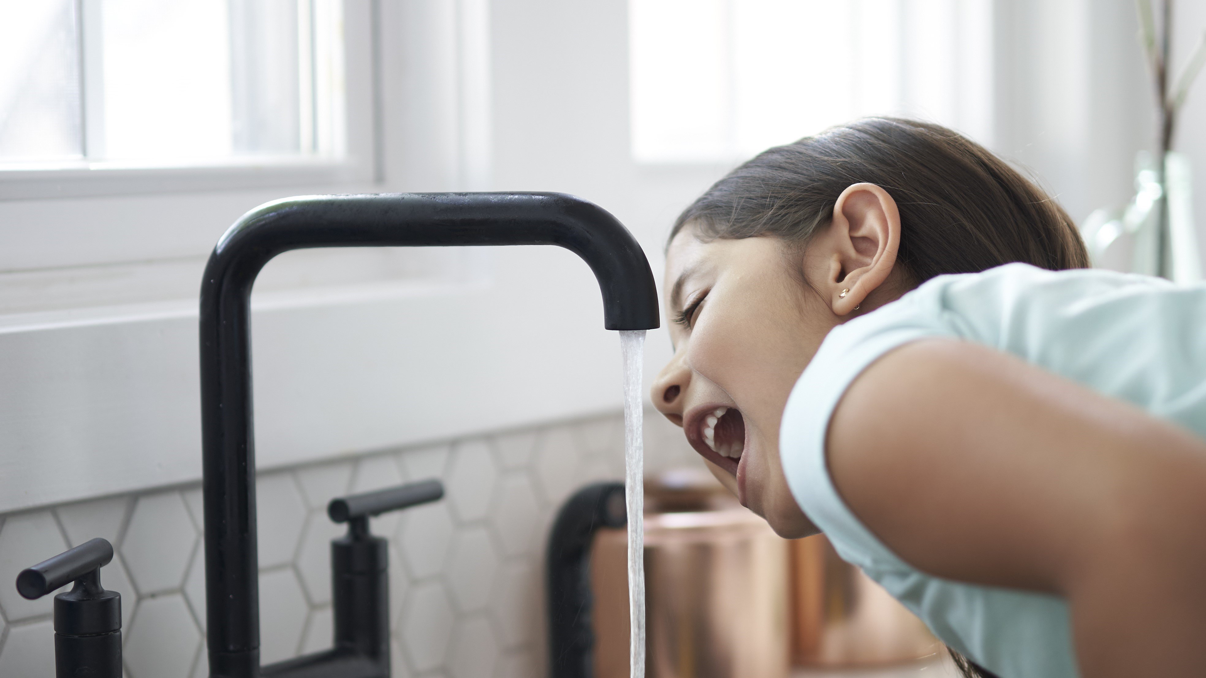 Young girl drinking water from a faucet