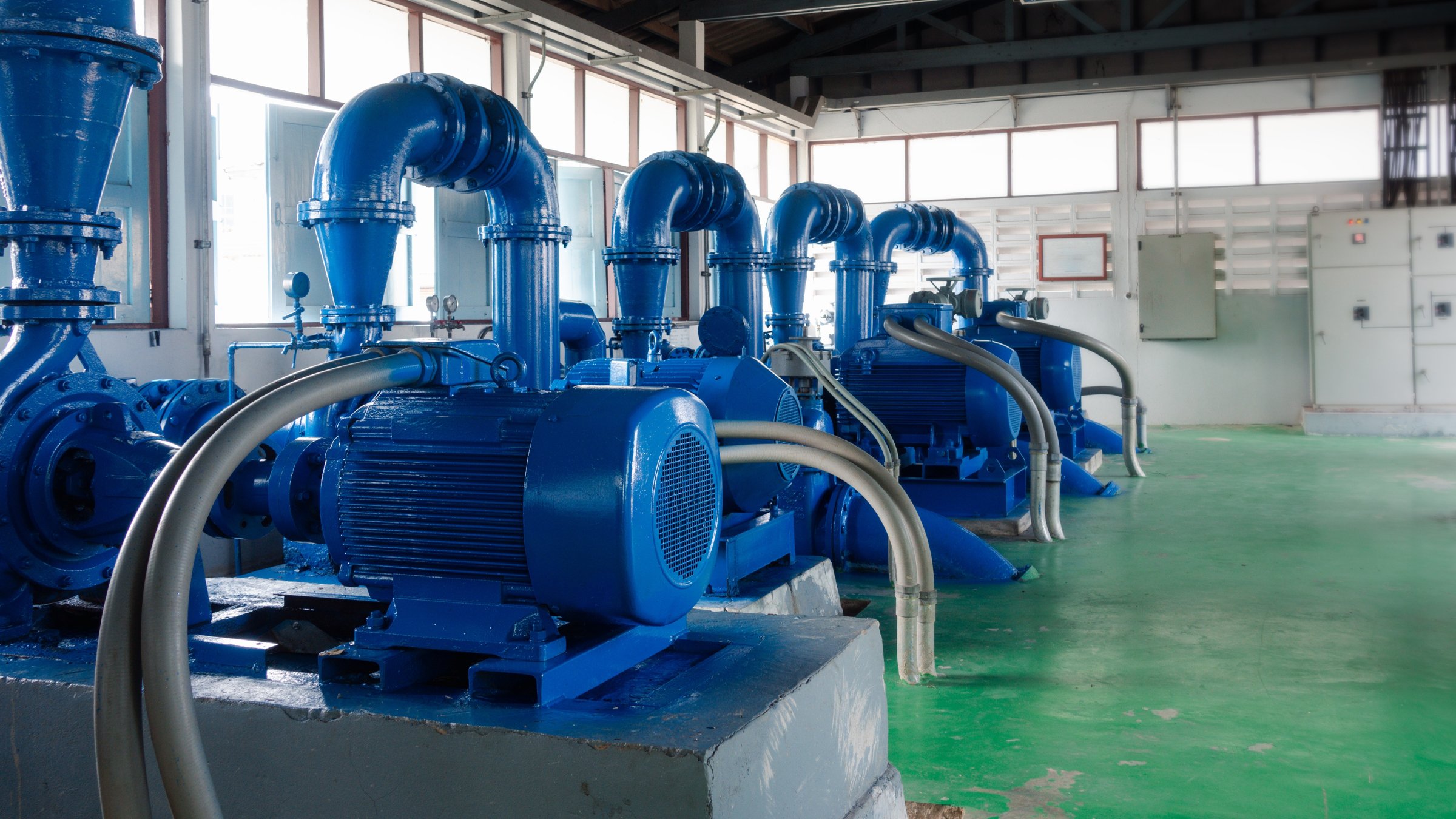 Blue electric motors drive water pumps in a large room with green floors within a water treatment facility
